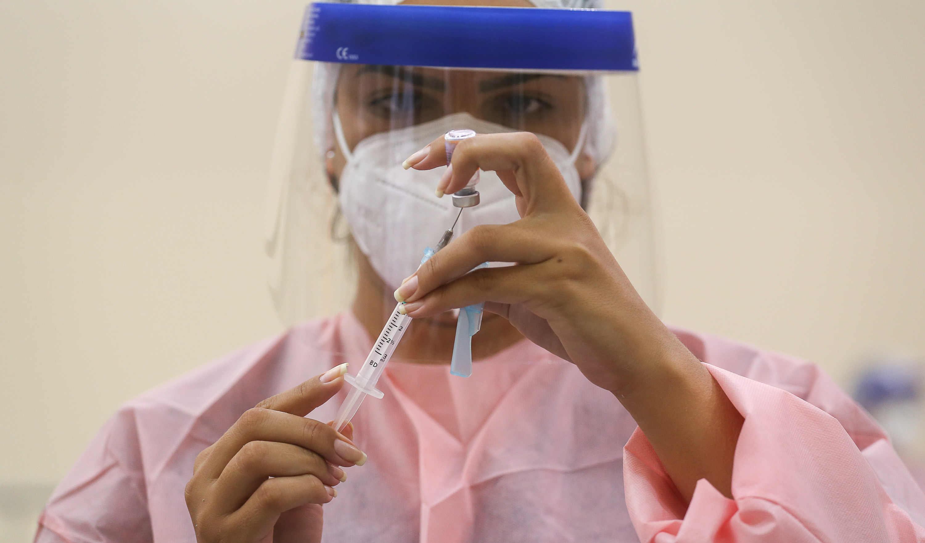 enfermeia usando EPIs manuseia uma seringa de vacina contra covid